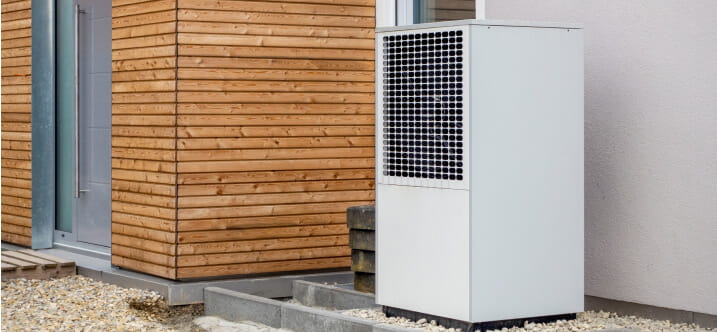 A heat pump sits at the side of a modern home on a cloudy day.
