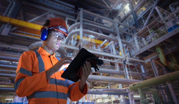 A technician using a tablet while standing in a large mechanical room.