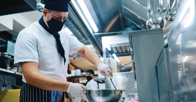 Male chef wearing protective mask cooking in a restaurant 