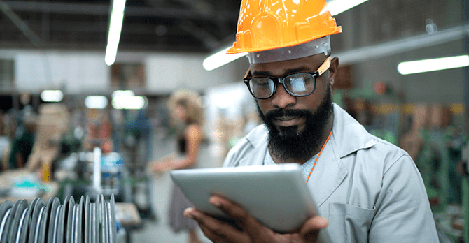 Man standing in factory wearing a hard hat looking at a tablet