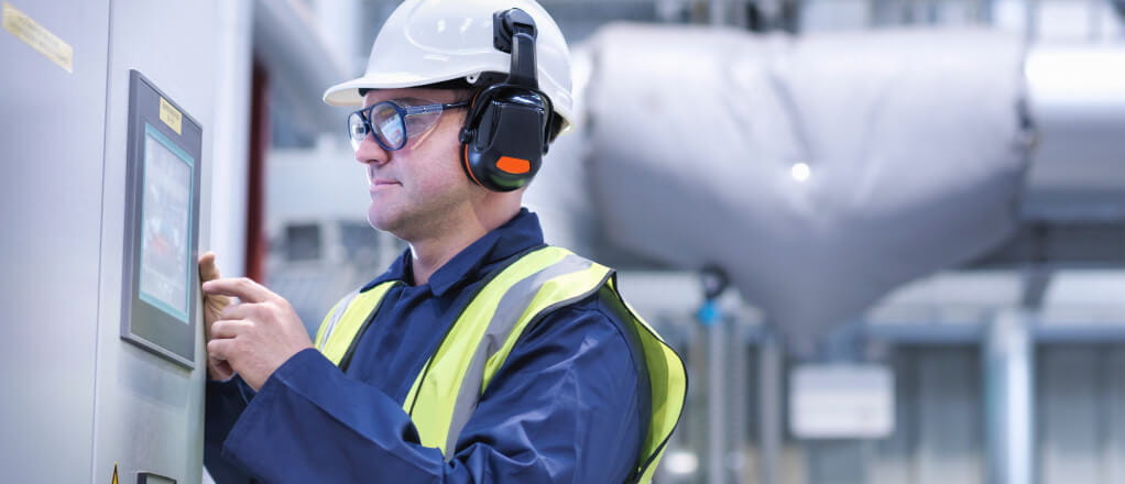 Man wearing hard hat and headphones using a touch screen in a power station