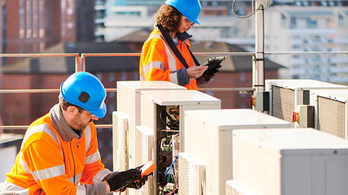 A man and woman in hard hats working on a rooftop air conditioning unit