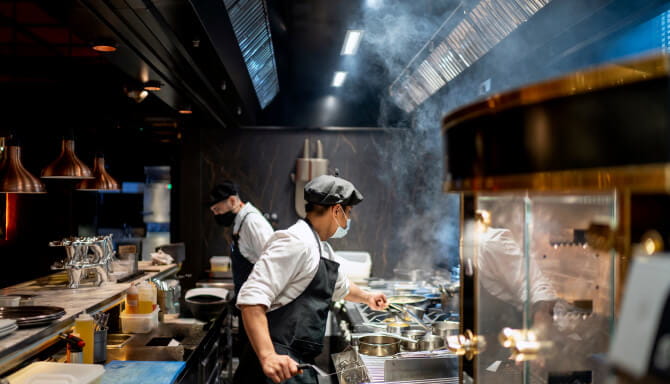 Two male chefs cooking in restaurant kitchen with protective face masks on
