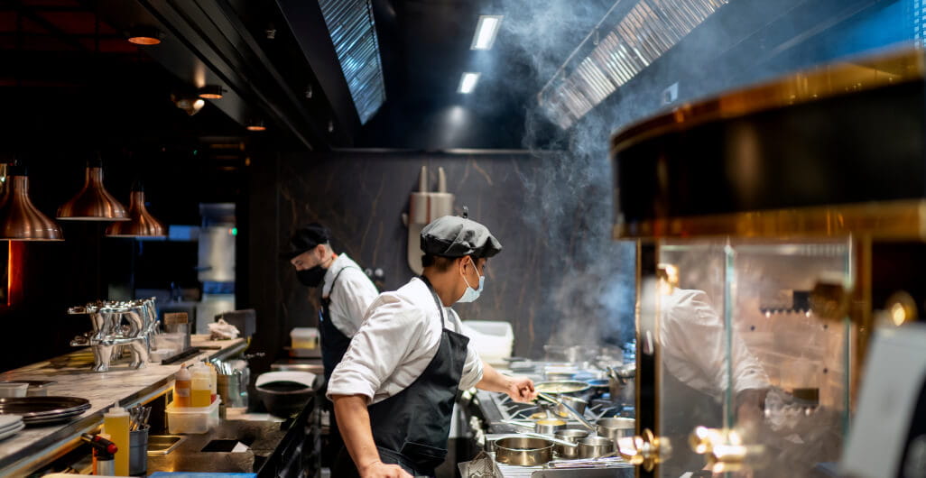 Two male chefs cooking in restaurant kitchen with protective face masks on