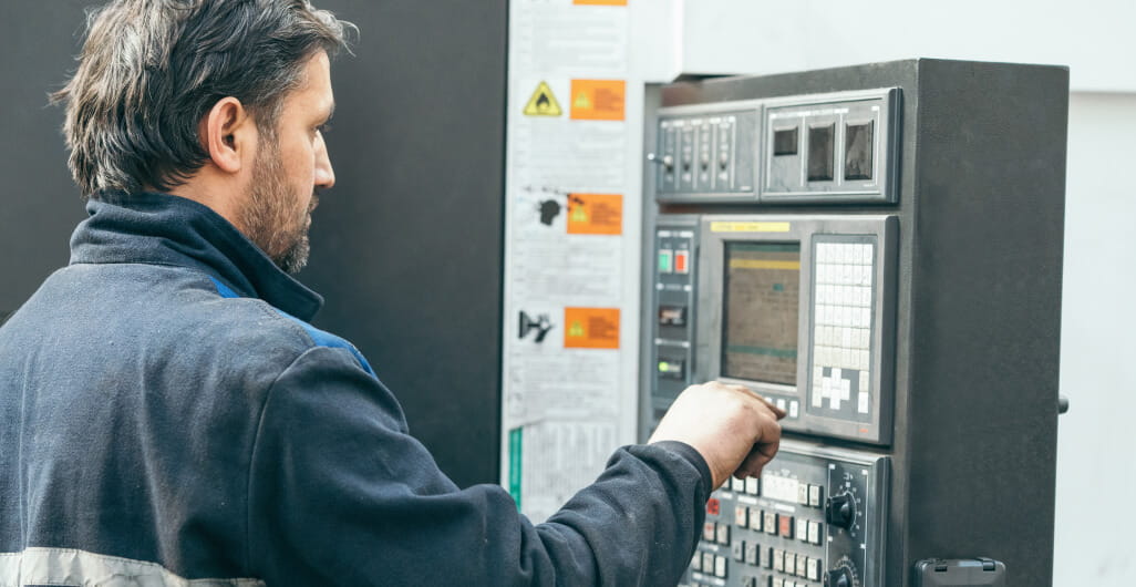 Man standing in front of programmable machine in factory