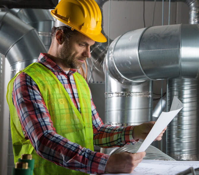 A man in a hard hat examining a blueprint in a factory