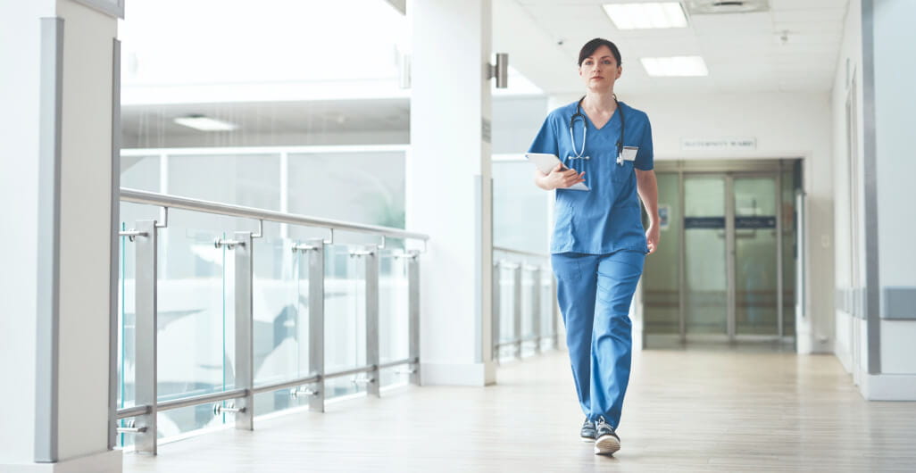 Female nurse in scrubs walking down hospital hallway