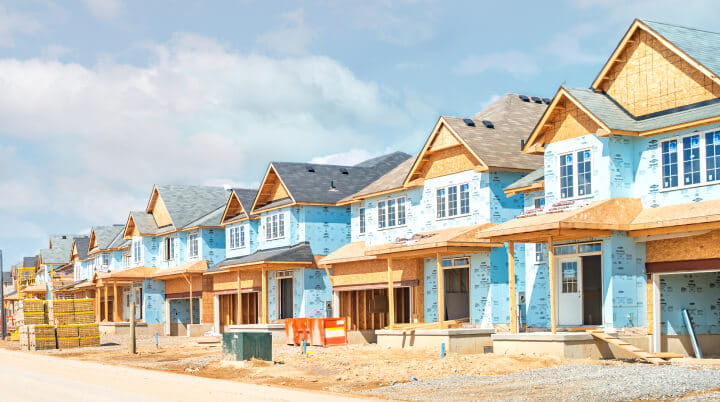 Street level view of a row of suburban homes under construction, on a sunny day. 