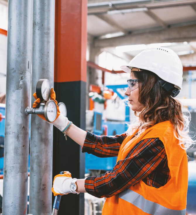 Woman in hard hat and protective googles inspecting valves in factory