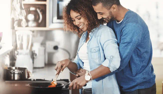 Man holding partner as she prepares a meal on the stove