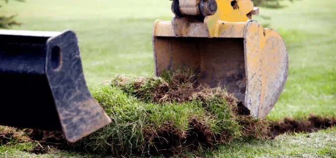 The bucket of a backhoe scooping up sod.