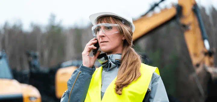 A contractor in safety gear taking a call on an excavation job site.