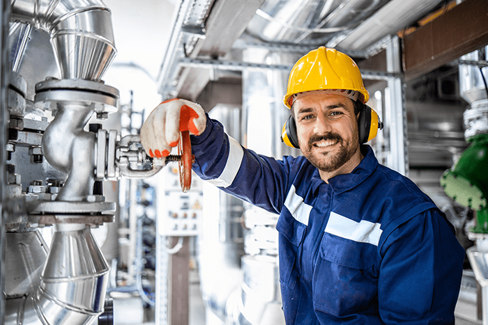 Portrait of smiling bearded refinery engineer or worker standing by pipes in an industry