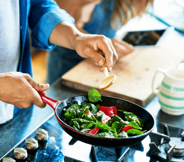 Person cooking vegetables in frying pan on a natural gas stove