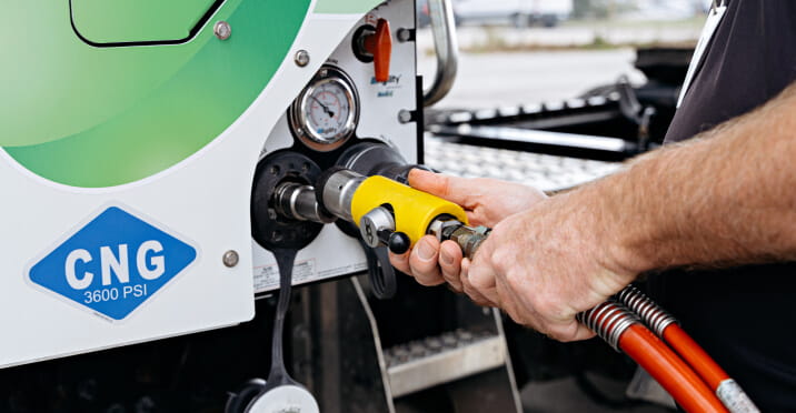 A person connecting a hose to a Compressed Natural Gas (CNG) pump.