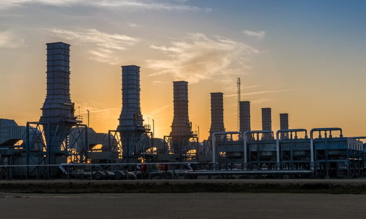 Photo of silhouettes of industrial energy plant structures, representing a production facility for low-carbon hydrogen.