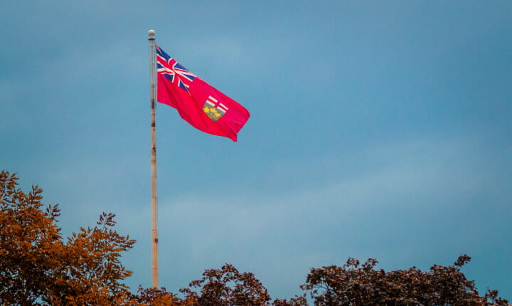 Photo of Ontario’s provincial flag waving in the breeze against a blue sky.