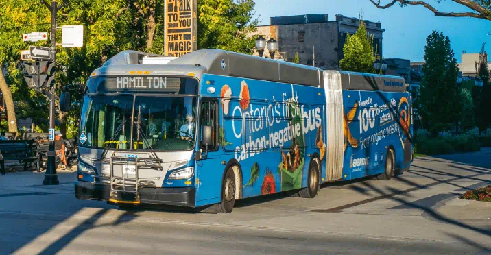 A public transit bus, wrapped with graphics indicating it is Ontario’s first carbon-negative bus, on the streets in Hamilton.
