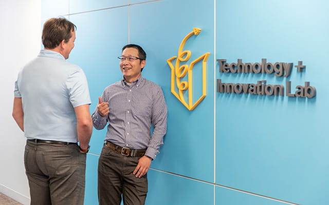 Two people standing next to a blue wall with a signage Technology + Innovation Lab
