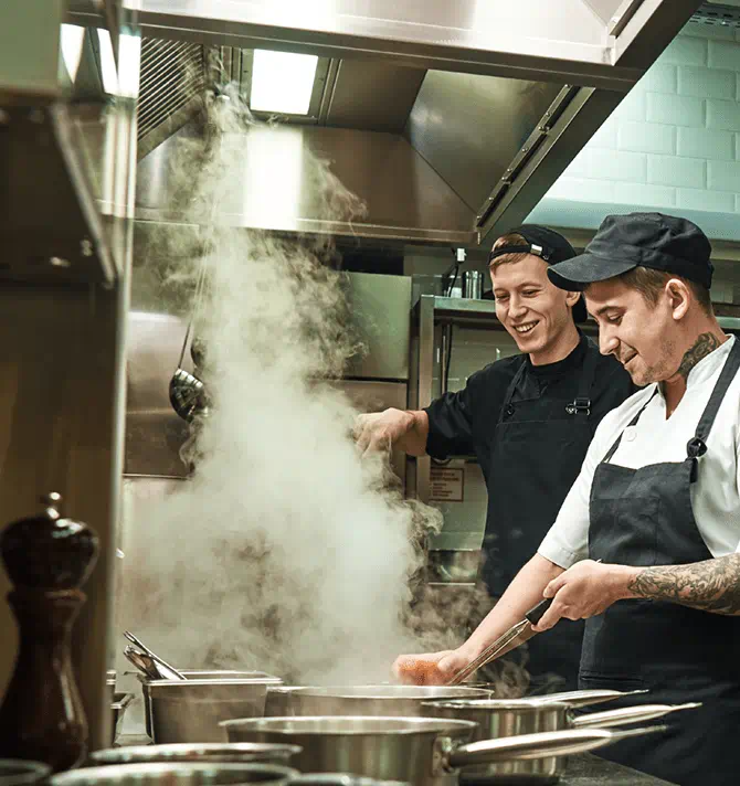 Two cheerful and smiling cooks in uniform preparing food in a restaurants' kitchen 