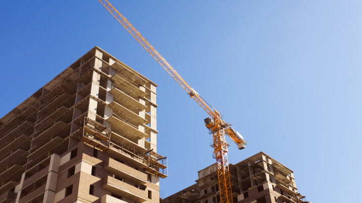 Two large condominium towers under construction on a clear day. A crane operates between the two buildings. 