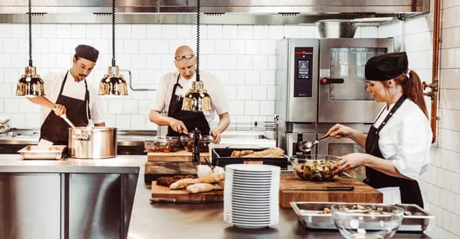Three cooks prepare food in a modern commercial kitchen.