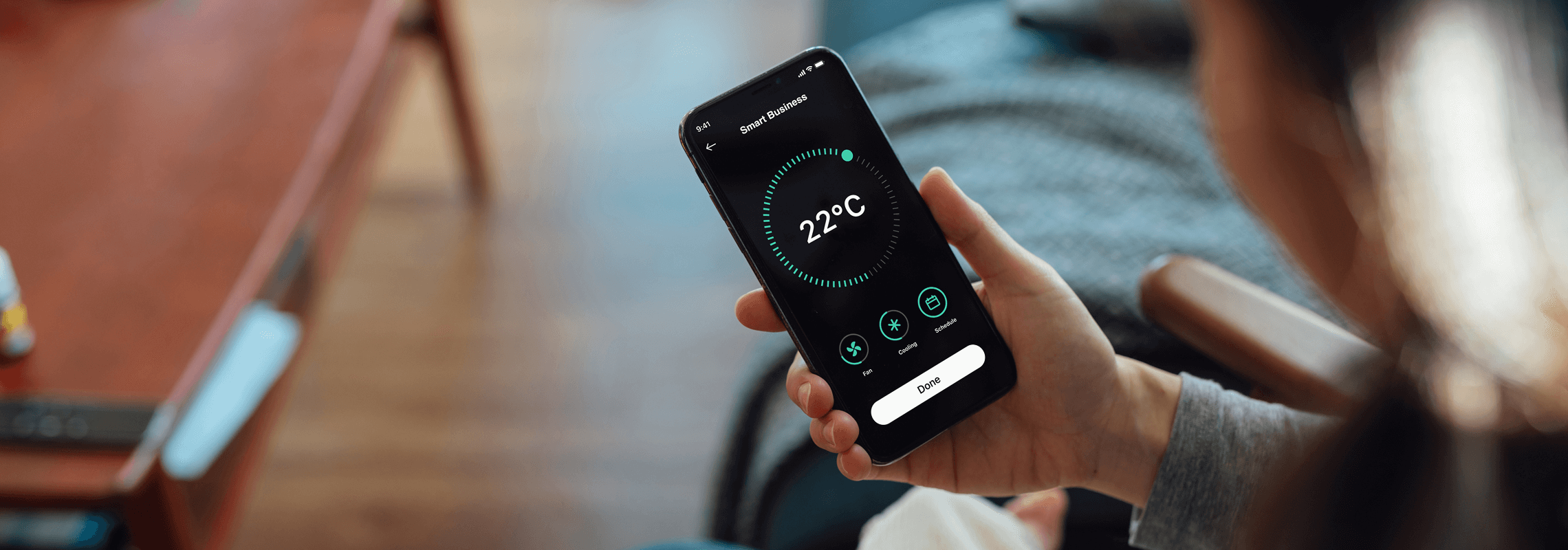 A person (blurred) views the temperature settings if their home using a smartphone app. The screen displays a temperature of 22°C.
