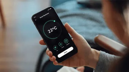 A person (blurred) views the temperature settings if their home using a smartphone app. The screen displays a temperature of 22°C.