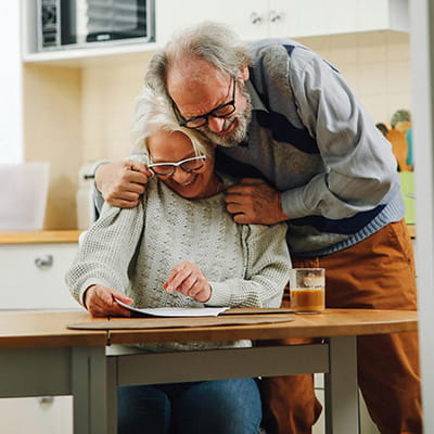 An elderly couple sharing a document at a kitchen table.