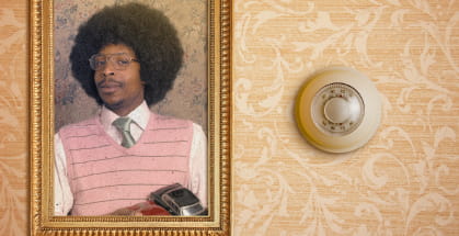 A floral wallpaper, picture of a man in ancient clothing in a frame and old thermostat on the wall.