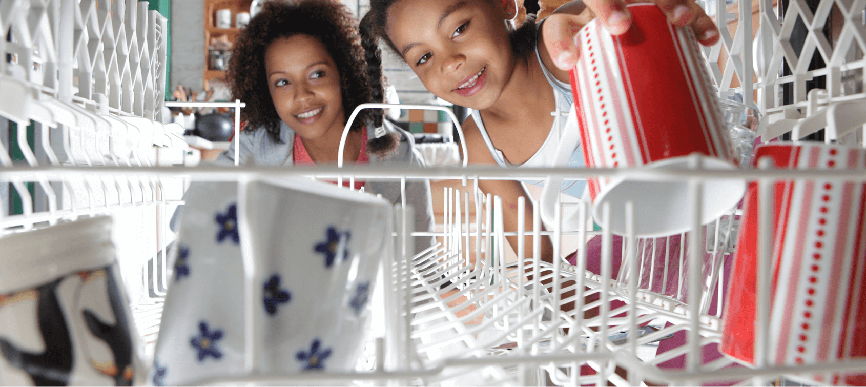 Mother overseeing young daughter load the dishwasher