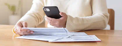 A person holding a mobile phone and paper bills.