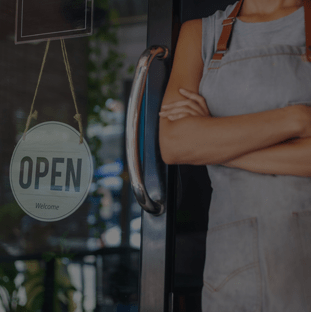 Owner of the cafe stands at the door with an open sign beside.