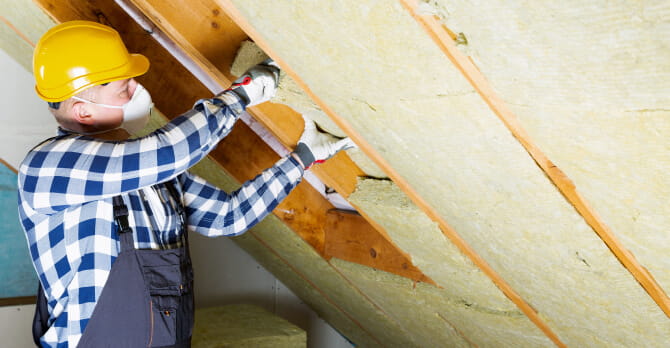 Man wearing hard hat and protective mask installing insulation in attic
